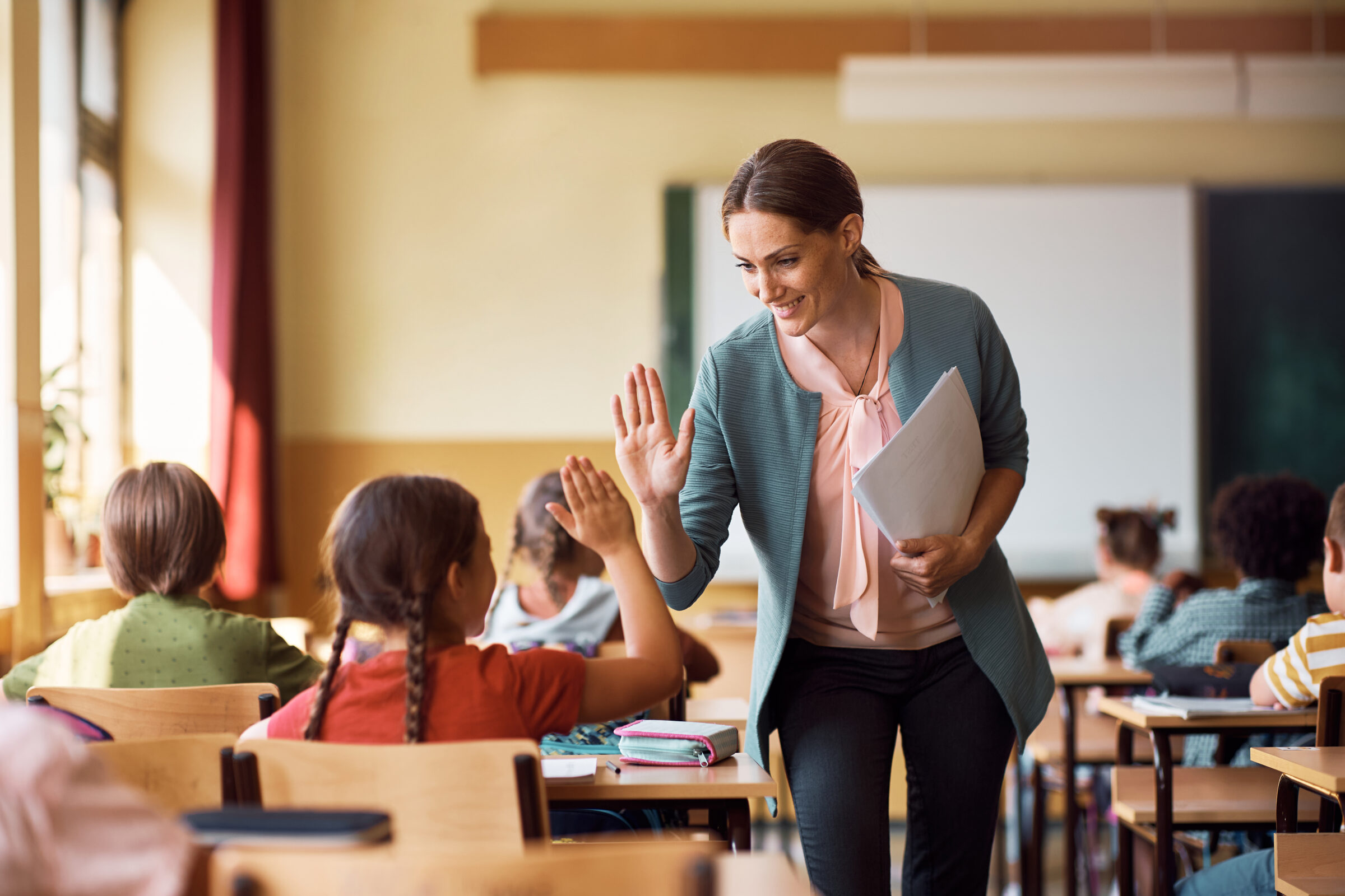 Happy teacher and schoolgirl giving high five during class at school.