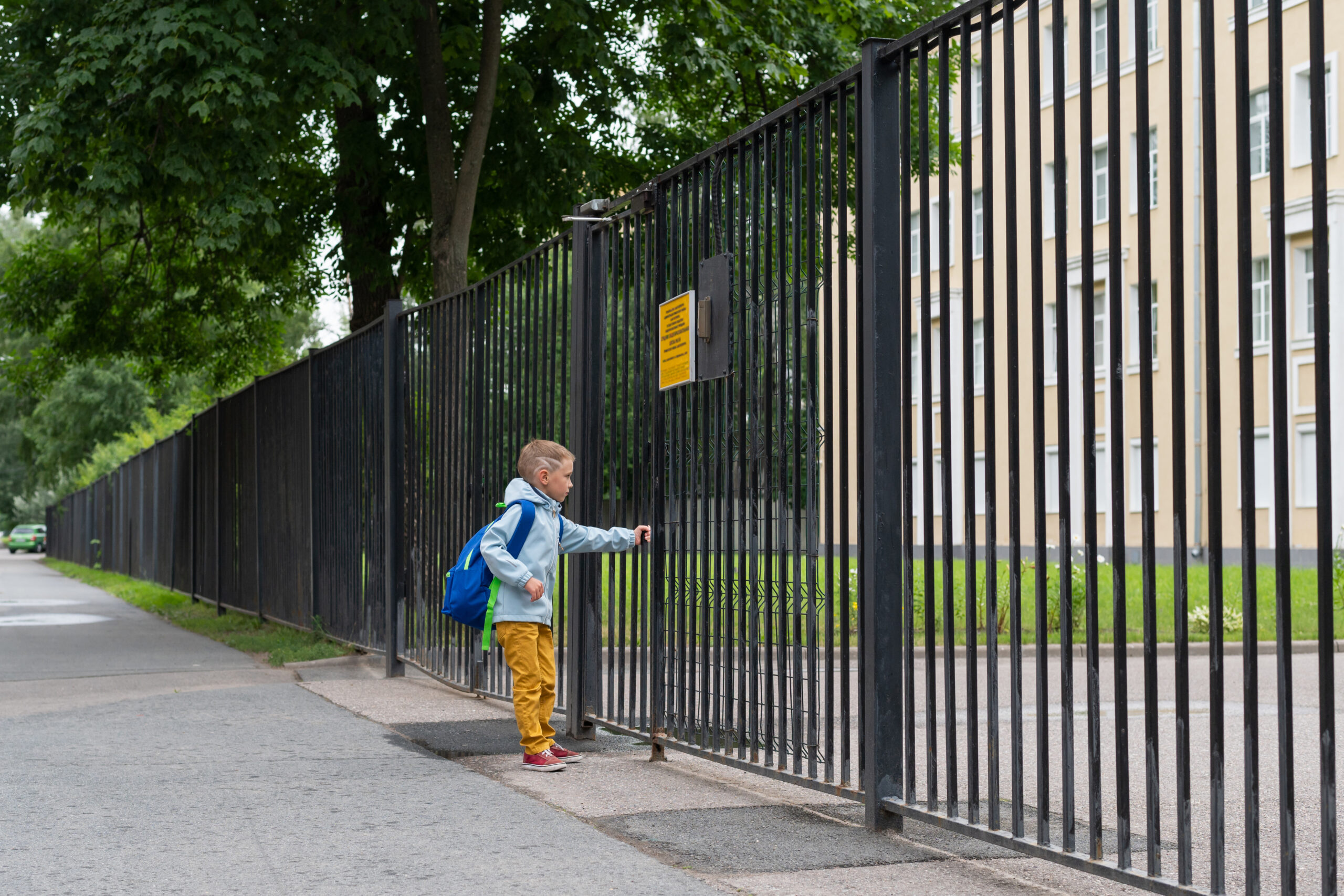 A boy is going to school for the first time. A boy with a bag goes to primary school. Child open gate to school. Back to school.