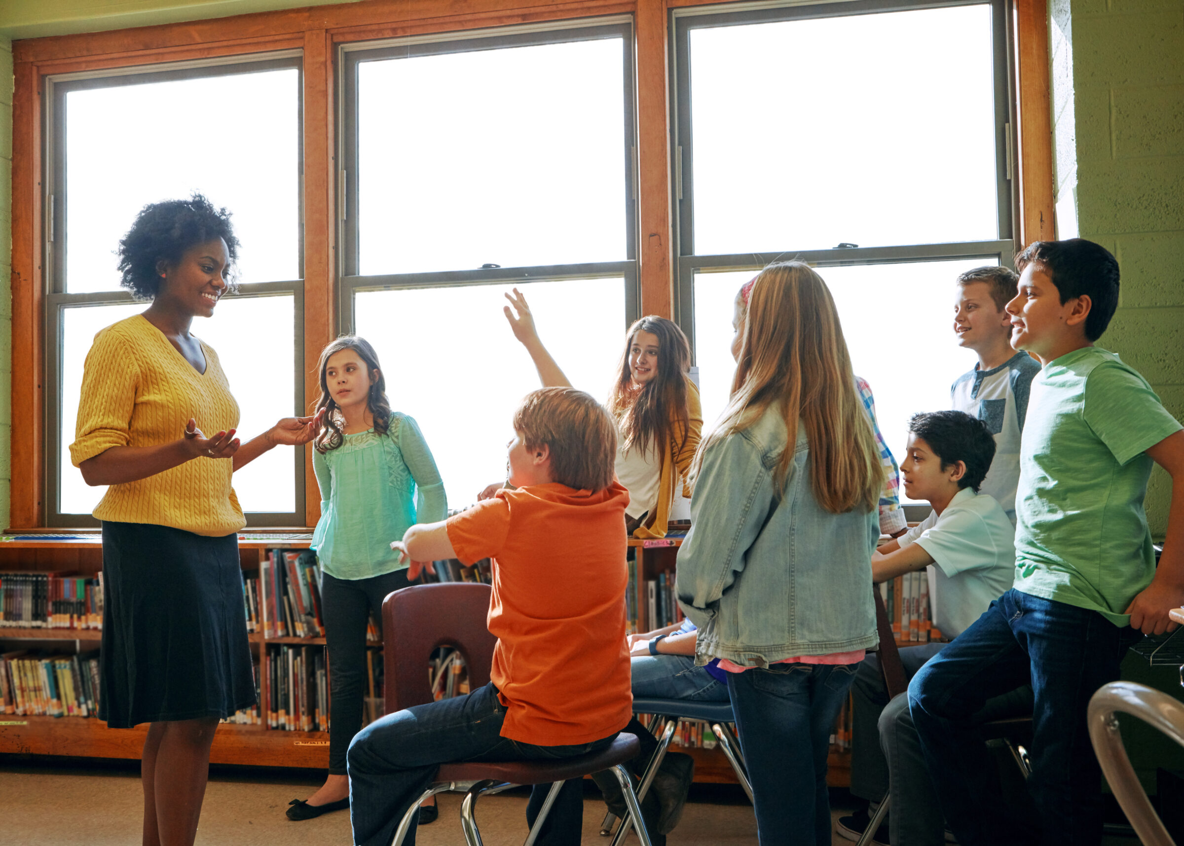 Learning, education and student with questions for teacher in middle school classroom. Library, scholarship group and male learner raising hand to answer question, studying or help with black woman.