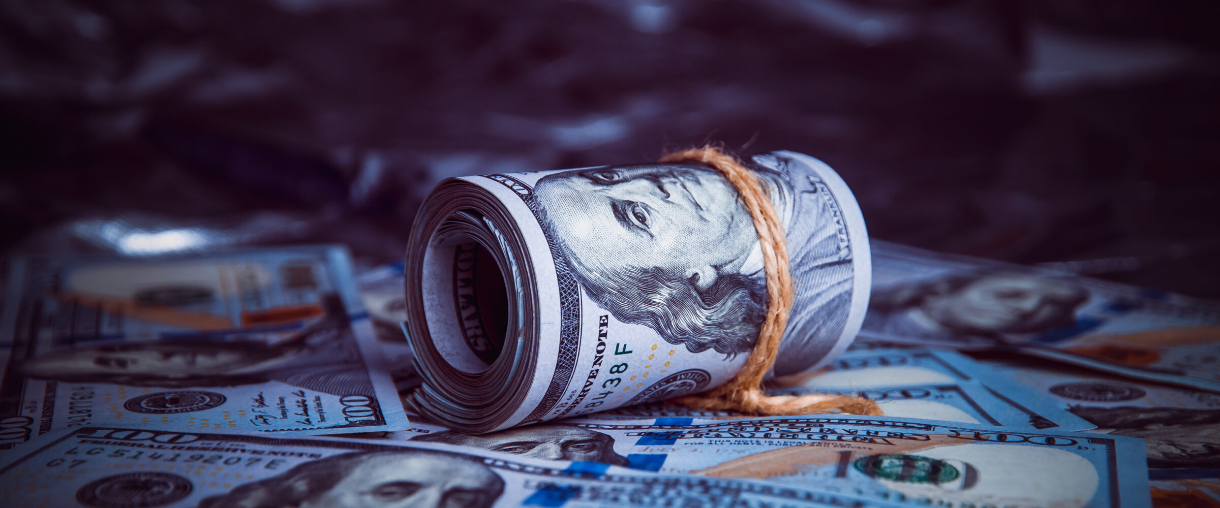 In the dark on broken money is a roll of dollars lit by a ray of light.