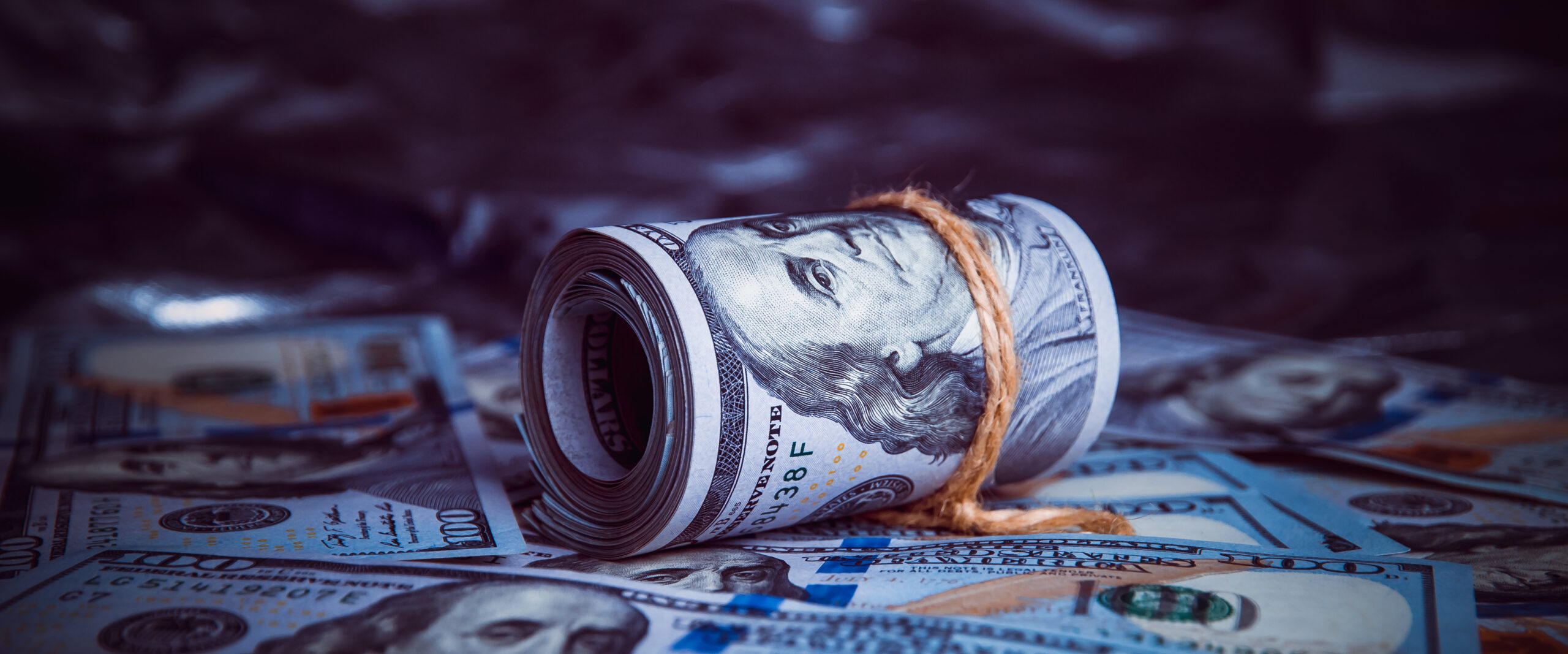 In the dark on broken money is a roll of dollars lit by a ray of light.