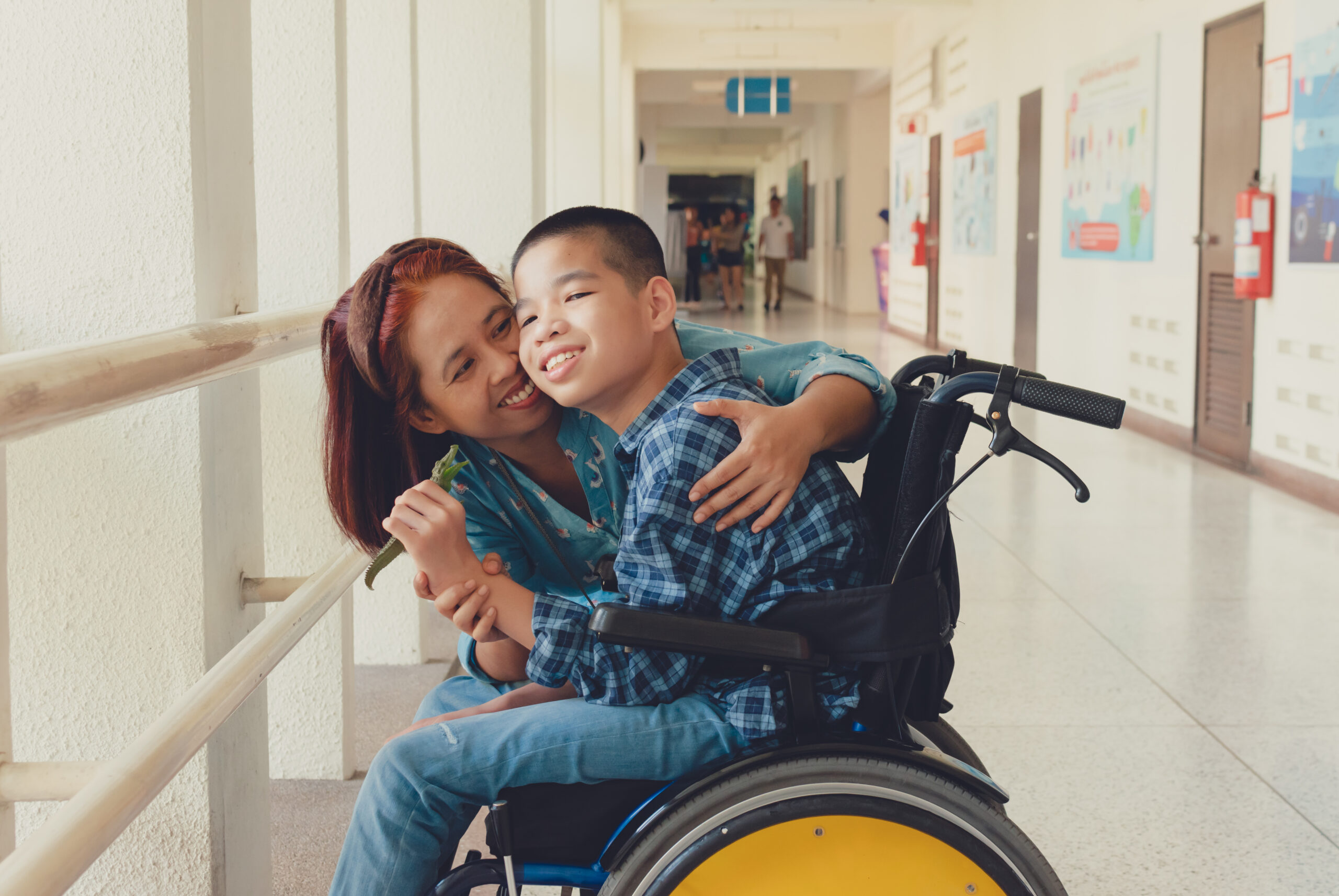 Mother and Asian special child on wheelchair is smile happily on background in school corridor, Life in the education age of disabled children, Happy disabled kid concept..