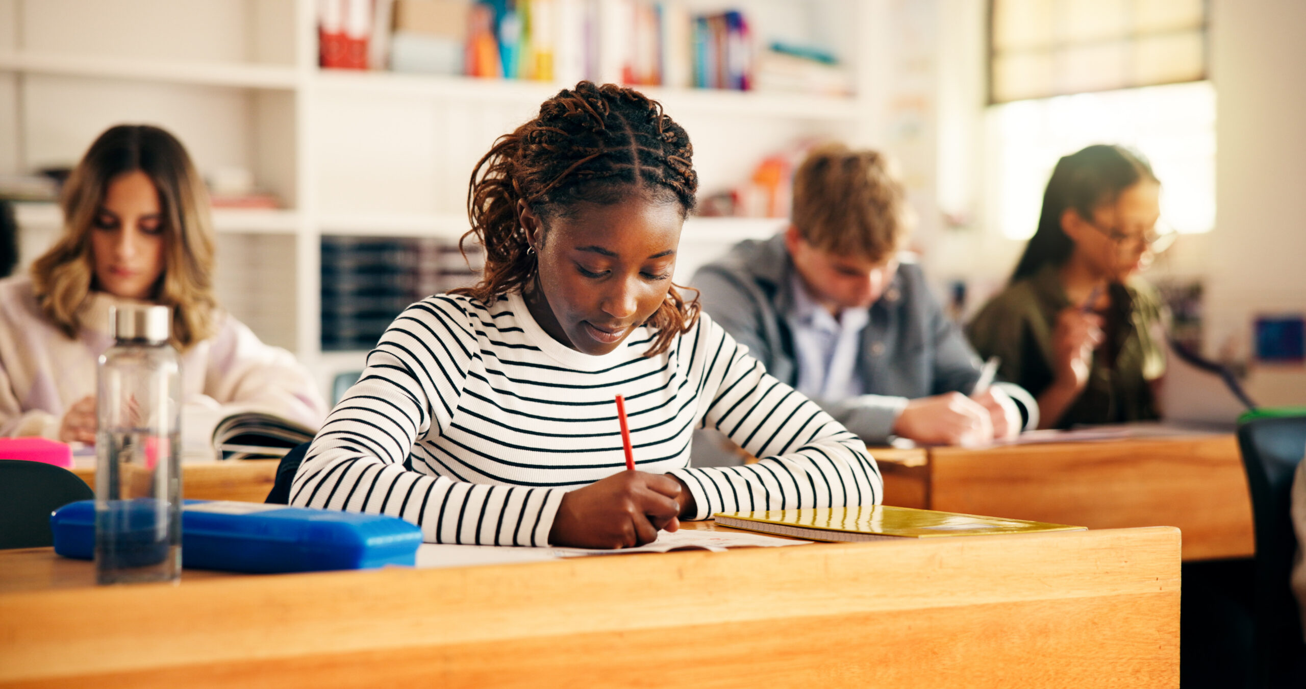 High school students, girl and writing on paper for exam assessment, quiz evaluation or learning. Teenager, education and group with aptitude test in classroom for scholarship, essay and development